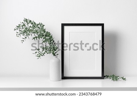 Portrait blank frame mockup in white interior with eucalyptus plant decoration in vase