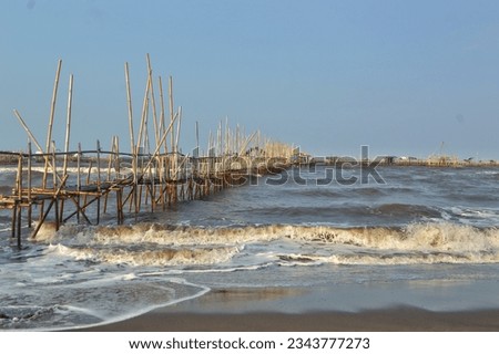 a view on the beach side with a bamboo wooden bridge that connects the fishing grounds
