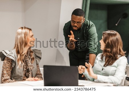 Front view photo of multiracial business people discussing at work. Good looking black male person explaining business strategy to his different aged female coworkers