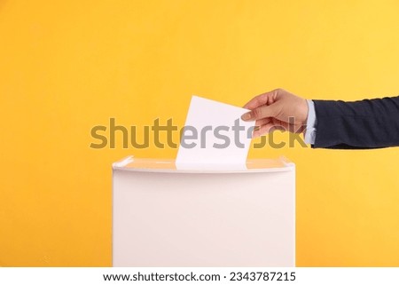 Woman putting her vote into ballot box on orange background, closeup Royalty-Free Stock Photo #2343787215