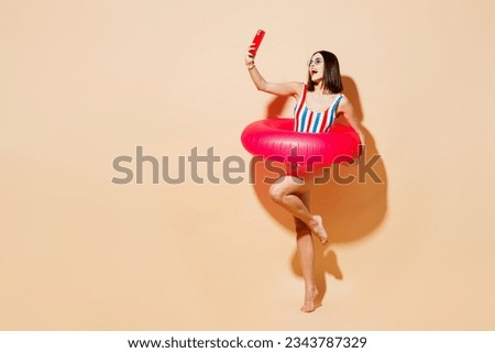Full body side view young woman wear one-piece swimsuit near hotel pool hold rubber ring do selfie shot on mobile cell phone isolated on plain beige background Summer vacation sea rest sun tan concept