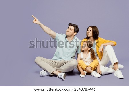 Full body young parents mom dad with child kid daughter girl 6 years old wear blue yellow casual clothes sit point index finger aside on area isolated on plain purple background. Family day concept