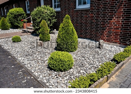 Beautiful decorative landscape design of shrubs and stones near a residential brick house in Germany.