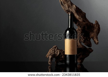 Bottle of red wine with old empty label. In the background old weathered snag. Black reflective background. Frontal view with space for your text.