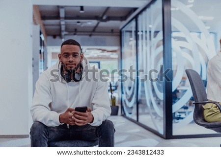 African American businessman wearing headphones while using a smartphone, fully engaged in his work at a modern office, showcasing focus, productivity, and contemporary professionalism Royalty-Free Stock Photo #2343812433