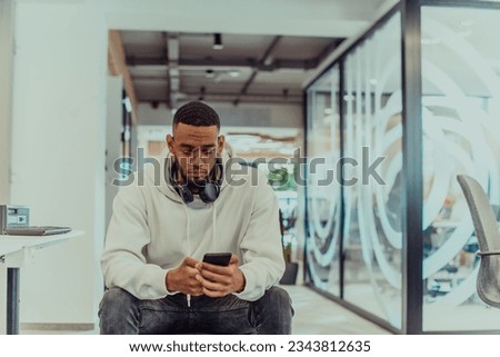African American businessman wearing headphones while using a smartphone, fully engaged in his work at a modern office, showcasing focus, productivity, and contemporary professionalism Royalty-Free Stock Photo #2343812635