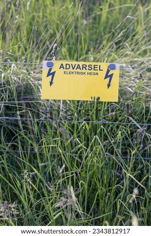 Warning - Electric fence guards a meadow and animals field. Summer season in Denmark Scandinavia