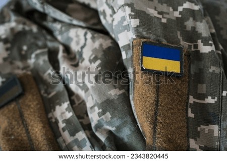 A banner of the Ukrainian flag on a military camouflage suit. Pixeled digital soldier's pixel camouflage uniform with ukrainian flag on chevron in blue and yellow colors. Ukrainian soldier uniform