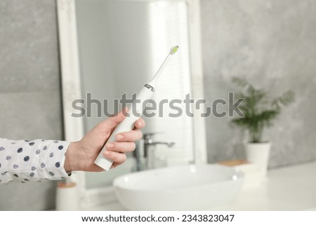 Woman holding electric toothbrush in bathroom at home, closeup