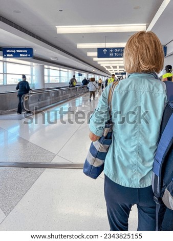Rear view of a mature woman walking through an airport with luggage in tow.  She is dressed casually. Located in Chicago, Illinois, USA at O'Hare International Airport.