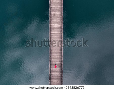 A woman walks on a wooden bridge that spans a lake. Aerial view Royalty-Free Stock Photo #2343826773