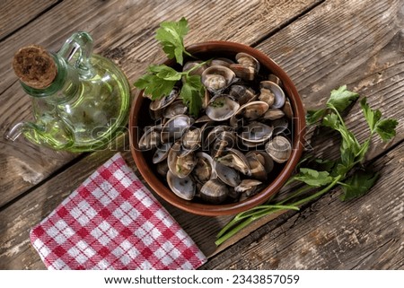 Grilled clam casserole on a vintage wooden table with red checkered napkin, parsley sprigs and oil can. top view