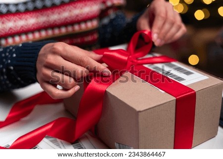 Merry Christmas shipping delivery concept. Santa Claus packing present box wrapping gift with red ribbon preparing post shipping delivery parcel. Close-up Royalty-Free Stock Photo #2343864467
