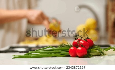 Close up view of woman in white shirt peeling a potato. Peel falling onto cutting board. Lady preparing potatoes to be cut and added to stock pot for dinner.