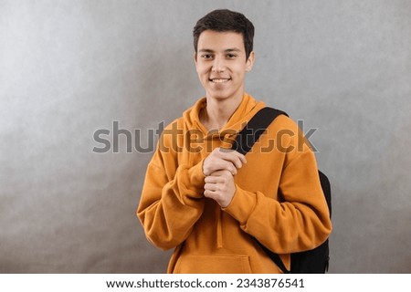 Portrait of a young student with a school bag. The teenager smiles and looks at the camera. A happy teenage boy on a grey background Royalty-Free Stock Photo #2343876541