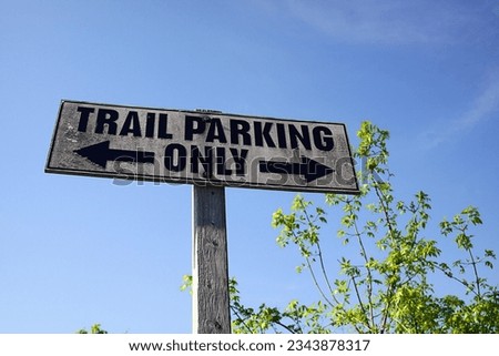 Trail Parking Only. Sign. Wooden post. Wood. Arrows. Direction. Blue sky. Summer. Outdoor activity. Hiking. Walking. Blue sky. Bushes. Weathered. Grungy. 