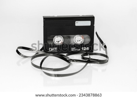 A DAT (Digital Audio Tape) cassette with twisted tape stands upright on a white background with reflection