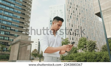 Young businessman typing on smartphone while standing in business district Royalty-Free Stock Photo #2343880367