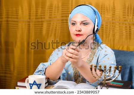 A Jewish woman in a kisui rosh headdress, a Torah teacher in headphones with a microphone, conducts an online lesson for women. Horizontal photo.