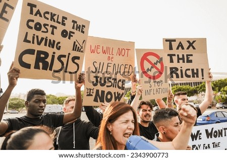 Crowd of multiracial people protest against inflation and financial crisis - Protesters marching for rise cost of living - Focus on banners