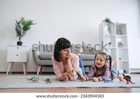 Close up view of affectionate mother and curious child being engaged in dinosaur play of plastic toys in lounge. Caring female parent sparking daughter's creativity by building own imaginary world. Royalty-Free Stock Photo #2343904583
