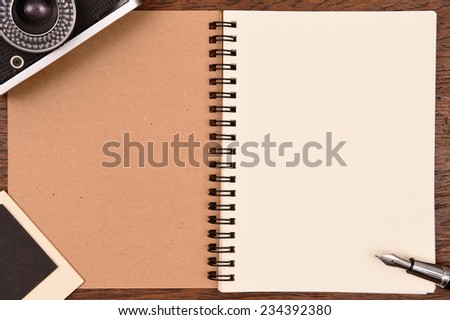 Blank notebook with pen, photo frames and camera on wooden background.