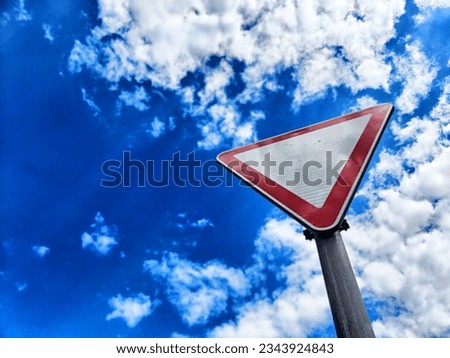Yield road sign. Red triangle on white background against a blue sky with white clouds. Traffic rules