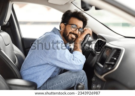 Automobile renting, buying, leasing. Thrilled young indian guy hugging steering wheel of his brand new car. Happy eastern man auto owner enjoying vehicle, lean on wheel with closed eyes and smiling Royalty-Free Stock Photo #2343926987