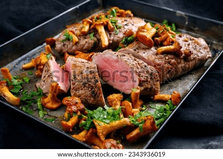 Fried dry aged pork fillet chateaubriand medallion steak natural with chanterelles and parsley served as close-up on a rustic metal tray on black background