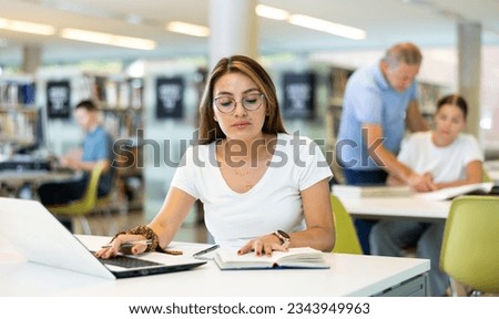Mexican school student girl doing research on project in the college library.. Royalty-Free Stock Photo #2343949963