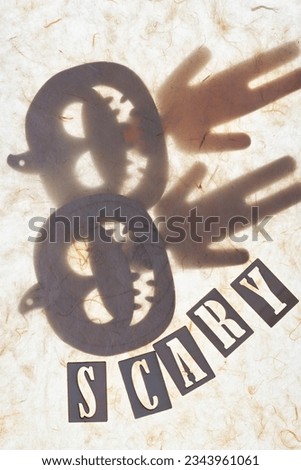pair of wooden halloween ornaments (jack o lantern and stick figure) and the word "scary" arranged under tissue paper and on an illuminated ground
