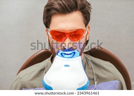 Portrait of handsome bearded middle aged man sitting in dental chair wearing red eyeglasses with open mouth, teeth whitening. Male patient in modern clean dentistry. Concept of dental treatment Royalty-Free Stock Photo #2343961461