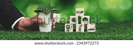 Businessman holding plant pot with ECO cube symbol. Forest regeneration and natural awareness. Ethical green business with eco-friendly policy utilizing renewable energy to preserve ecology. Alter Royalty-Free Stock Photo #2343972273