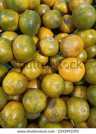 A true-to-life picture capturing a collection of yellow oranges, a few marked with black spots, taking up the frame.
