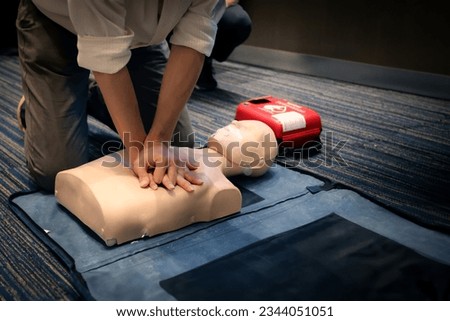 Asian man practicing CPR on a plastic mannequin with Automated External Defibrillator (AED) on the floor. Basic rescue and first aid training. Royalty-Free Stock Photo #2344051051