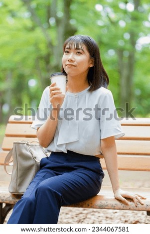 Japanese woman with drink sitting on the bench in park