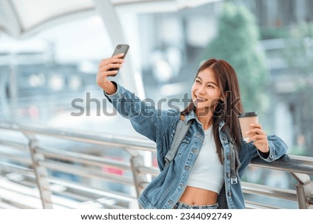 Happy young asian woman taking selfie photo on mobile phone at city, female using smartphone camera for self portrait outside.