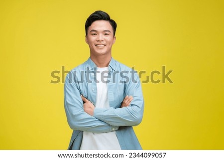 Smiling handsome man in blue polo shirt standing with crossed arms isolated on yellow background