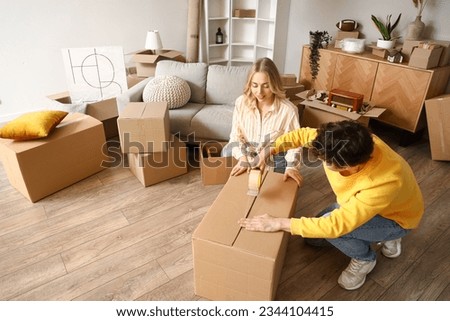 Young couple taping cardboard box in room on moving day Royalty-Free Stock Photo #2344104415