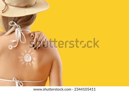 Young woman with sun made of sunscreen cream on her back against yellow background Royalty-Free Stock Photo #2344105411