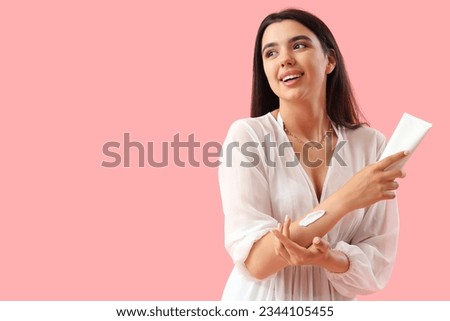 Young woman applying sunscreen cream on pink background Royalty-Free Stock Photo #2344105455