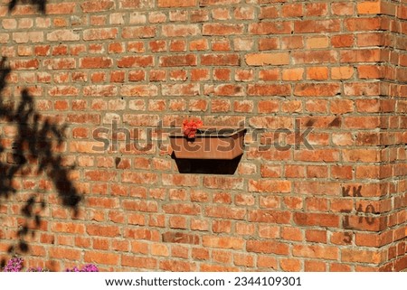 A flower pot hangs on an old wall of a red brick house