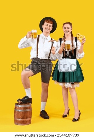 Young couple in traditional German clothes with beer and snacks on yellow background Royalty-Free Stock Photo #2344109939