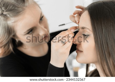 Photo conveys energy and warmth moment when makeup artist in beauty salon applies minor cosmetic corrections on client's eyebrows. All this to create unique image that emphasizes its natural beauty.