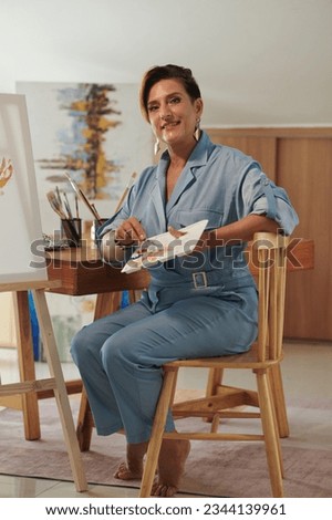 Cheerful mature painter mixing paints when creating new masterpiece