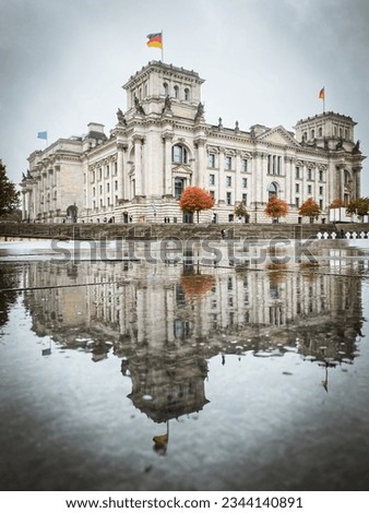 Low angle view of reflecting Reichstag building, seat of the German Parliament (Deutscher Bundestag), in Berlin, Germany with trees in autumn color against cloudy sky Royalty-Free Stock Photo #2344140891