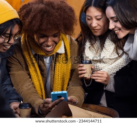 Group of multiethnic friends with mobile phone having fun while drinking coffee during winter in a city