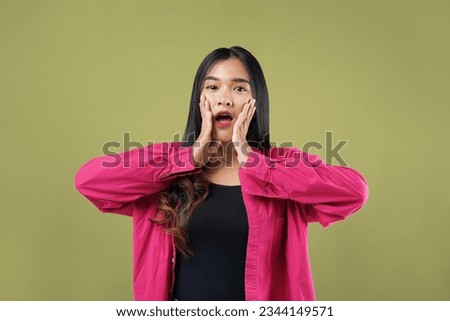 Photo of young asian woman wearing casual afraid and shocked, surprise and amazed expression with hands on face, isolated on green background