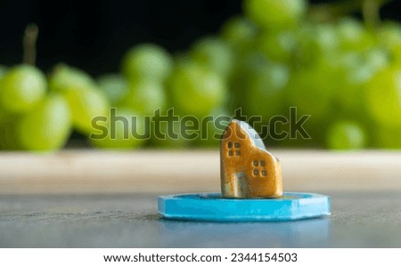 Miniature ceramic house, on a blurry background with green grapes. Orange cute toy building
