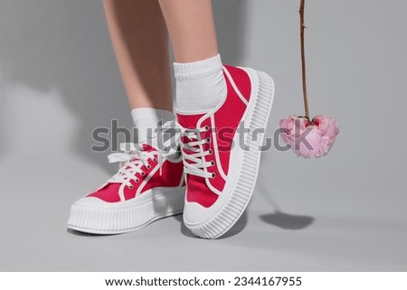 Woman posing in red classic old school sneakers with beautiful flower on light gray background, closeup